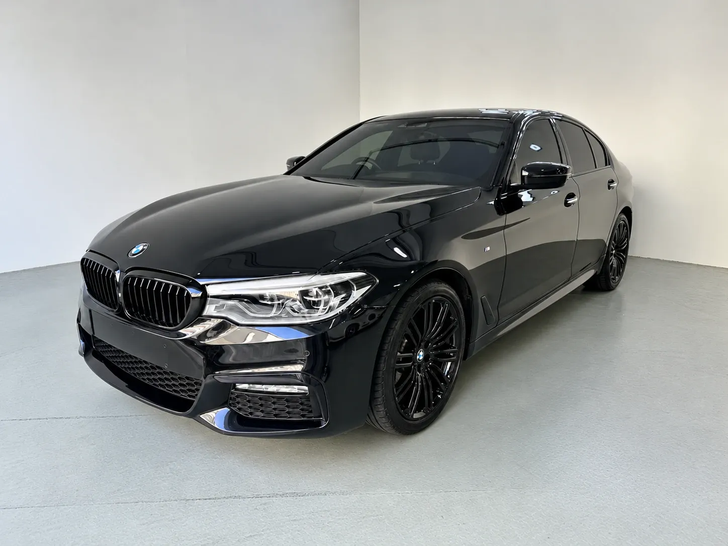 Black 2019 BMW 530i M Sport (G30) with black wheels, parked in a white studio